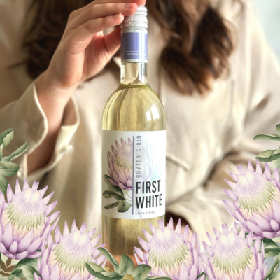 Weibliche Person hält Ruyter's Bin First White Weißweinflasche in den Händen. Im Vordergrund sind Protea Blumen zu sehen, die auch das Label der Flasche zieren
