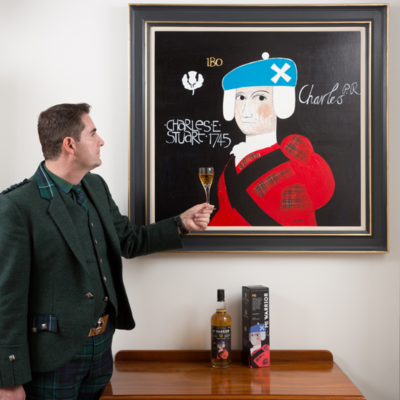 Antony McClallum vor einem Kunstwerk stehend. In der linken Hand hält er ein Glas Whisky